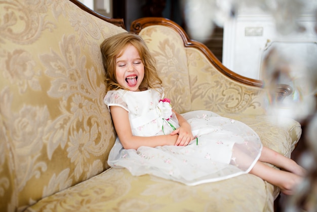 mała blond dziewczyna w kolorowej sukni siedzi na dużej kanapie.
