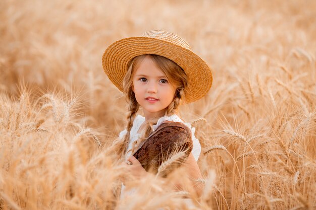 mała blondynka trzyma świeży bochenek chleba w polu pszenicy w lecie