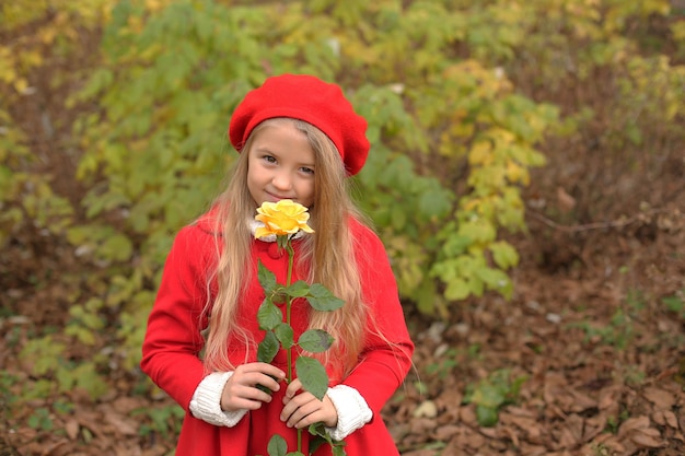 mała blondynka w czerwonym płaszczu i berecie trzyma w rękach żółtą różę