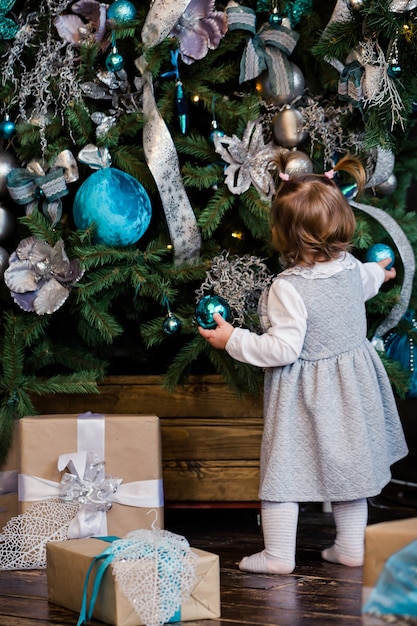 Zdjęcie mała córeczka udekoruje choinkę w domu. koncepcja rodziny, x-mas, ferii zimowych i ludzi. rodzina z dzieckiem świętuje ferie zimowe.