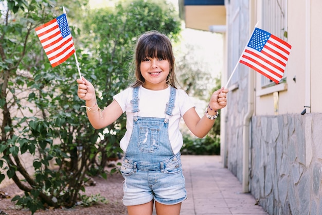 Mała czarnowłosa dziewczynka z amerykańskimi flagami w ogrodzie swojego domu Koncepcja obchodów dnia niepodległości 4 lipca patriotyzm wakacje i amerykańska duma