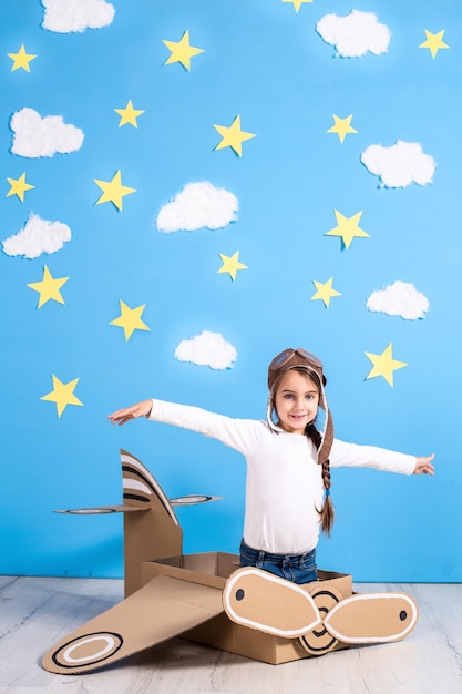 Mała Dziewczyna Marzyciel Bawi Się Tekturowym Samolotem W Studio Na Tle Błękitnego Nieba I Białych Chmur.