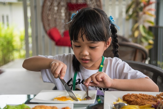 Mała dziewczynka azjatycka je smażone jajko na danie przy stole