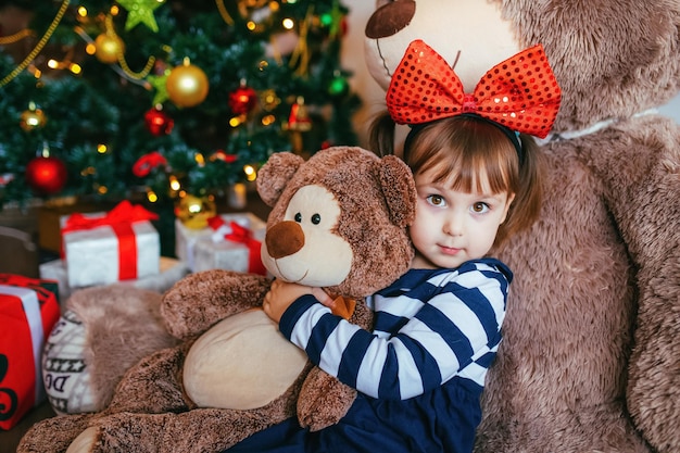 Mała dziewczynka bawi się leżąc na misiu podarowanym przez Świętego Mikołaja na Boże Narodzenie Nowy rok wystrój