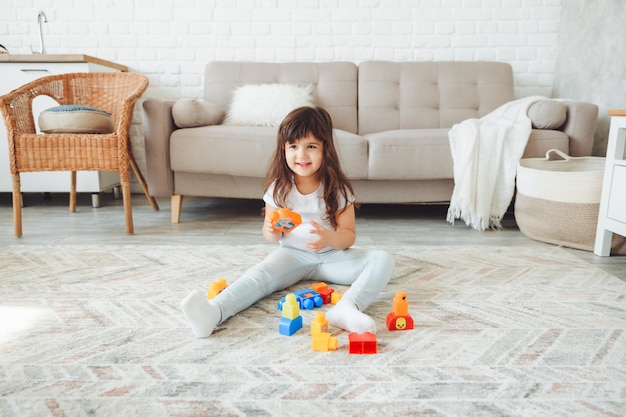 Mała dziewczynka bawi się w domu na podłodze z kolorowym konstruktorem