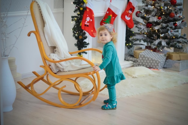 Mała dziewczynka bawiąca się w pokoju z dekoracją świąteczną w bujanym fotelu