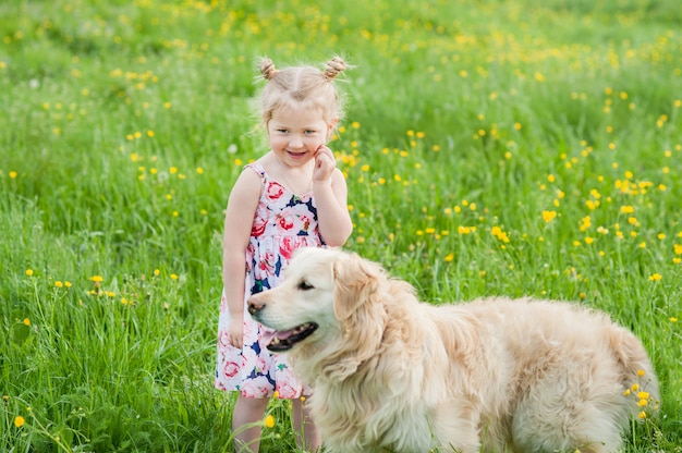Mała dziewczynka bawić się z golden retriever na świeżej trawy łące z żółtymi kwiatami