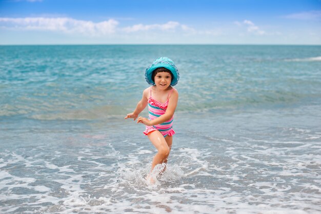 Mała dziewczynka biegnie po plaży na falach morza z odpryskami.