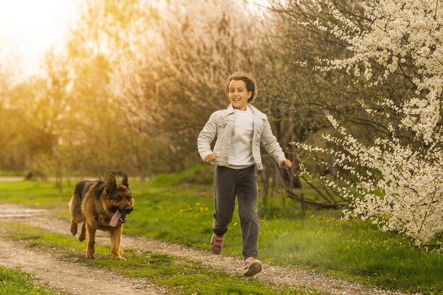 Mała dziewczynka biegnie z psem w ogrodzie kwiatowym