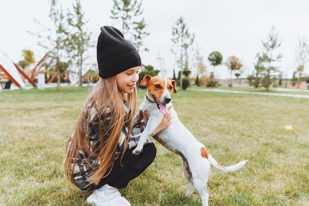 Mała dziewczynka całuje i przytula swojego psa rasy Jack Russell Terrier w parku Miłość między właścicielem a psem dziecko trzyma psa w ramionach