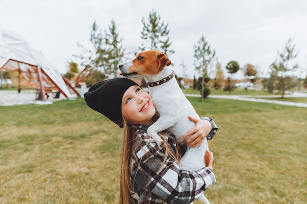 Mała dziewczynka całuje i przytula swojego psa rasy Jack Russell Terrier w parku Miłość między właścicielem a psem dziecko trzyma psa w ramionach