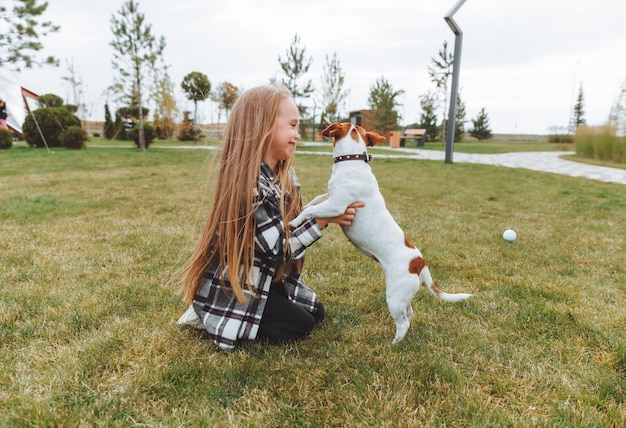 Mała dziewczynka całuje i przytula swojego psa rasy Jack Russell Terrier w parku Miłość między właścicielem a psem dziecko trzyma psa w ramionach