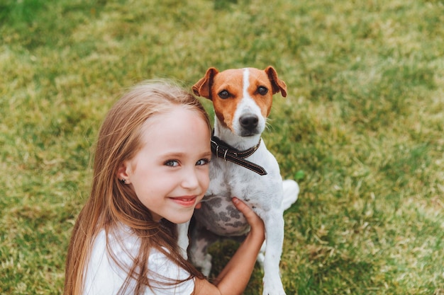 Mała dziewczynka całuje i przytula swojego psa rasy Jack Russell Terrier w parku Miłość między właścicielem a psem dziecko trzyma psa w ramionach