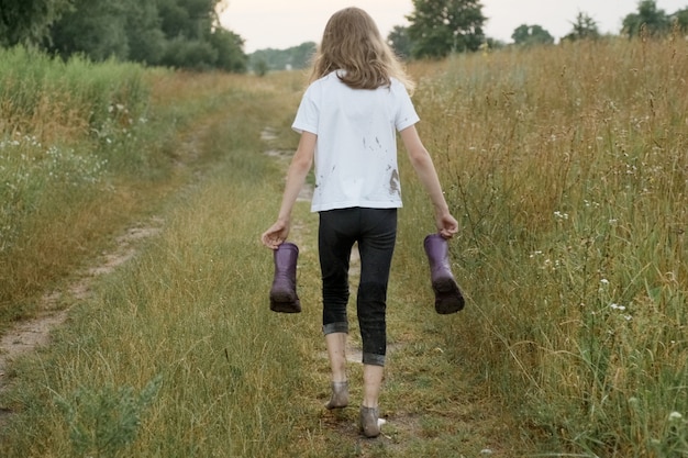 Mała dziewczynka chodzenie na wiejskiej drodze z kalosze w ręce