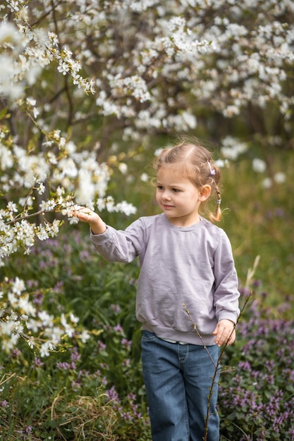 Mała dziewczynka cieszy się ładnym i słonecznym wiosennym dniem w pobliżu kwitnącej jabłoni w praskim parku