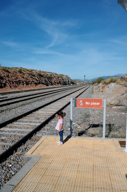 Zdjęcie mała dziewczynka czeka na pociąg przy torach na stacji na wolnym powietrzu