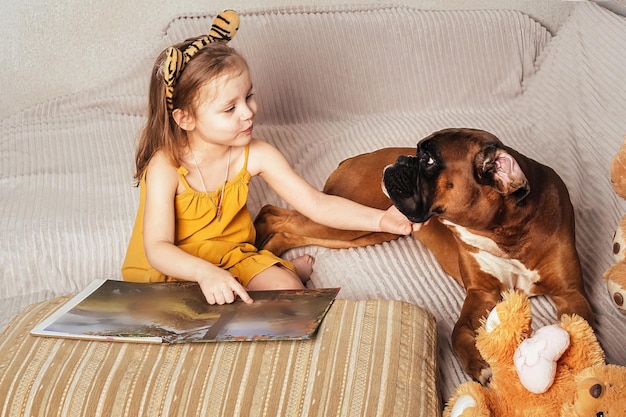 mała dziewczynka czyta książkę swojemu dużemu psu na kanapie i pokazuje zdjęcia