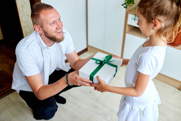 Mała dziewczynka daje swojemu przystojnemu ojcu pudełko na dzień ojca, uśmiechając się córka gratulując tacie i dając prezent na urodziny w domu. Kocham Cię tato. Szczęśliwego dnia ojca.