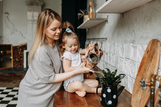 Zdjęcie mała dziewczynka dba o nawadnianie kwiatu w garnku siedzącym na szafce kuchennej w domu