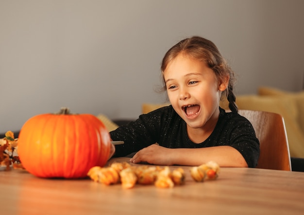 Mała Dziewczynka Dekoruje Dynię W Pokoju Na Halloween. Dzieci Dekorują Dom. Dzieci Rzeźbią Dynię. Upiorna Zabawa Na Halloween