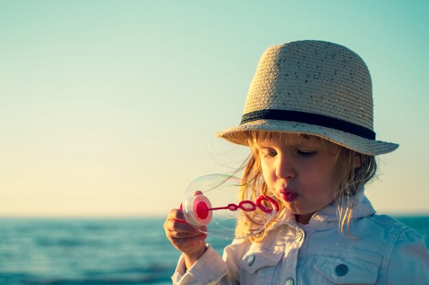 Mała dziewczynka dmucha mydlanych bąble przy morzem. Stonowane zdjęcie