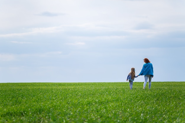 Mała dziewczynka dziecko i matka kobieta biegają i skaczą, zielona trawa na polu, słoneczna wiosenna pogoda, uśmiech i radość dziecka, błękitne niebo z chmurami