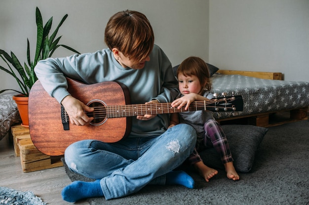 Mała dziewczynka gra na gitarze z mamą na podłodze w domu