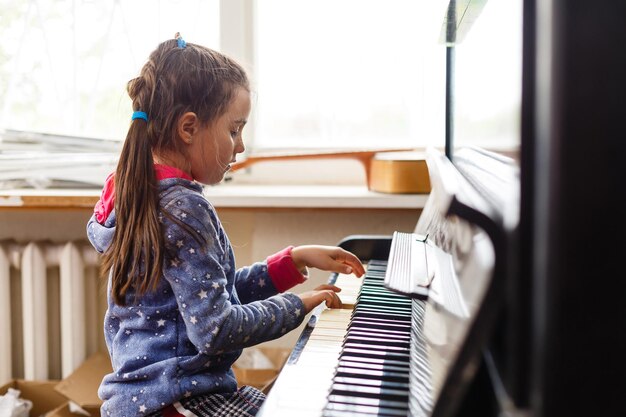 mała dziewczynka gra na starym pianinie w starym domu