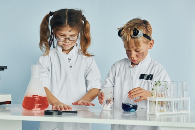 Mała dziewczynka i chłopiec w białych fartuchach bawią się w naukowców w laboratorium, używając sprzętu