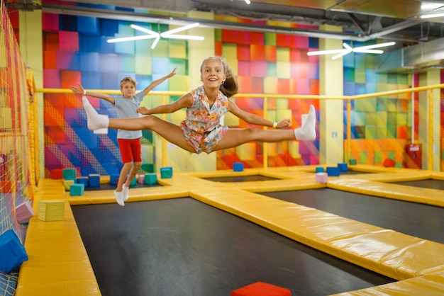 Mała dziewczynka i chłopiec, zabawy na trampolinie dla dzieci, plac zabaw w centrum rozrywki.