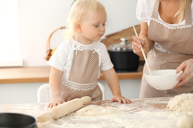 Mała dziewczynka i jej blond mama w beżowych fartuchach bawią się i śmieją podczas wyrabiania ciasta w kuchni. Domowe ciasto na chleb, pizzę lub upiecz ciasteczka. Rodzinna zabawa i koncepcja gotowania.