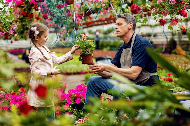 Mała dziewczynka i jej ojciec opiekują się kwiatami doniczkowymi w szkółce roślin Skupiamy się na człowieku