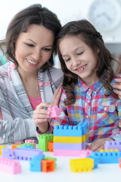 Mała dziewczynka i mama bawią się kolorowymi plastikowymi klockami w domu