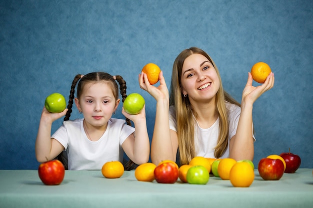 Mała dziewczynka i mama bawią się owocami i wygłupiają. Noszą t-shirty