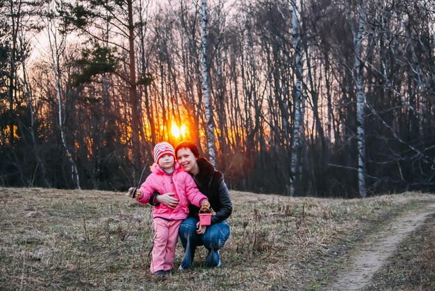 Mała dziewczynka i szczęśliwa mama spacerują po lesie wczesną wiosną Jasny zachód słońca