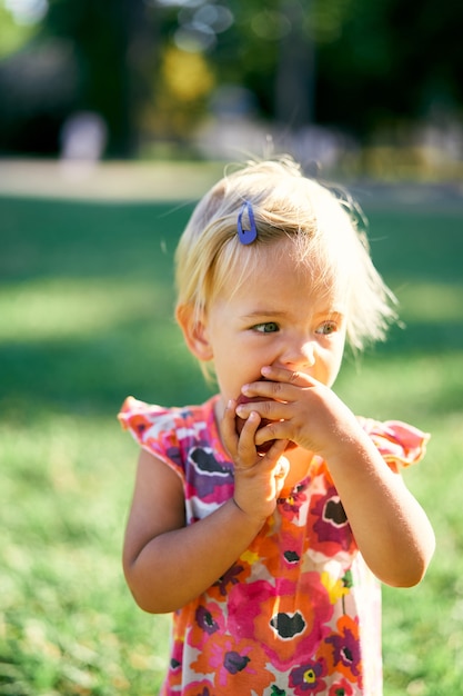 Mała dziewczynka je brzoskwinię na portretie na zielonym trawniku