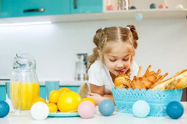 Mała dziewczynka je śniadanie w kuchni z rogalikami i sokiem pomarańczowym.