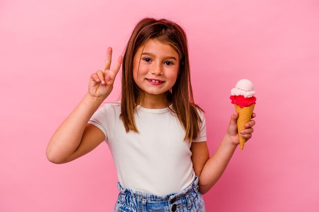 Mała Dziewczynka Kaukaski Trzymając Lody Na Białym Tle Na Różowy Radosny I Beztroski Pokazuje Palcami Symbol Pokoju.