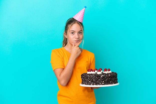 Mała dziewczynka kaukaski trzymająca tort urodzinowy na białym tle na myślenie o niebieskim tle