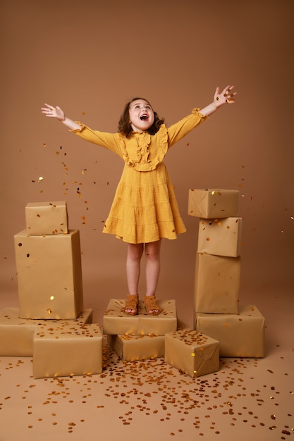 Mała dziewczynka kręcone ze stosem prezentów na święta i złotym konfetti