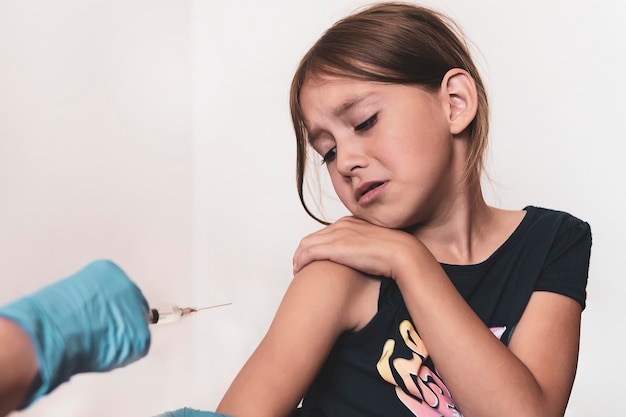 Mała dziewczynka krzyczy ze strachu, że zostanie postrzelona w ramię. Szczepienia przeciwko groźnym chorobom wirusowym. Zapobieganie i ochrona przed wirusami. Wstrzyknięcie przeciwciał. Pojęcie medyczne.