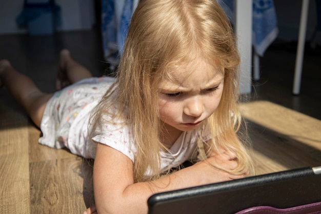 Zdjęcie mała dziewczynka leżąca na podłodze i patrząca na tablet