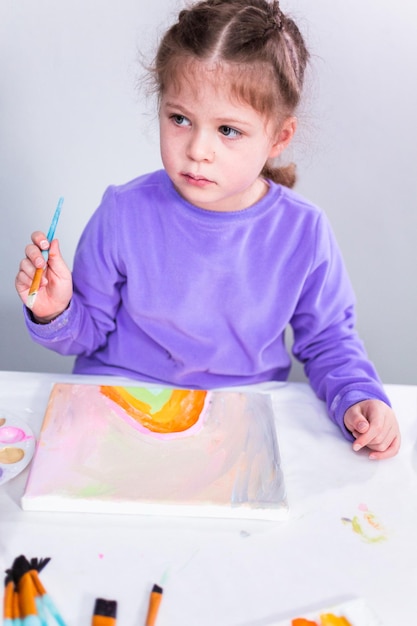 Mała dziewczynka maluje na płótnie farbą akrylową.