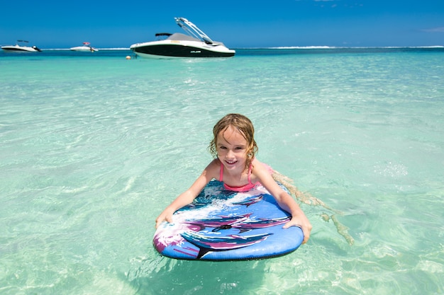 Mała dziewczynka - młody surfer z bodyboardem świetnie się bawi na małych falach oceanu. Aktywny styl życia rodziny