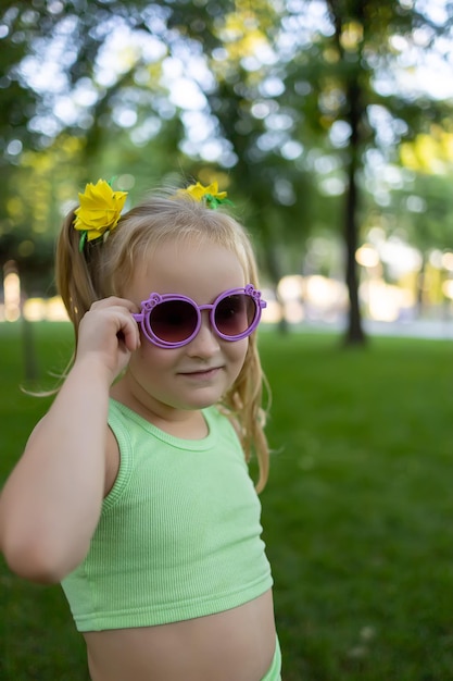 Mała dziewczynka model trzyma okulary i pozuje do kamery w parku