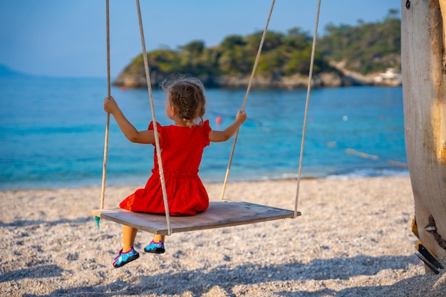 Mała dziewczynka na drewnianej huśtawce na letnich wakacjach na plaży oludeniz w turcji oludeniz dziewczynka jeździ na huśtawce