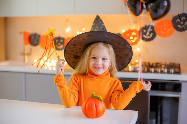 Mała dziewczynka na Halloween w stroju wiedźmy z dynią w domu w kuchni