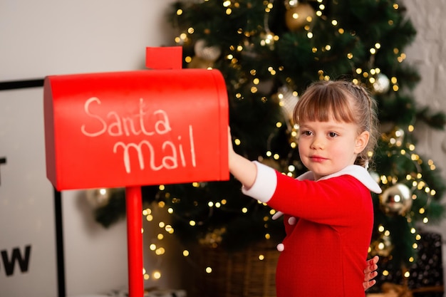 Mała dziewczynka napisała list do Świętego Mikołaja z życzeniami i umieściła go w czerwonym pudełku. Skoncentruj się na dziecku