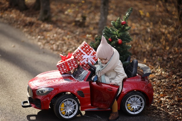 mała dziewczynka nosi choinkę i prezenty w czerwonym samochodzie