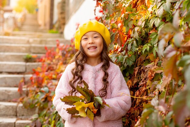Mała dziewczynka o azjatyckim wyglądzie w jesiennych pięknych liściach trzyma bukiet